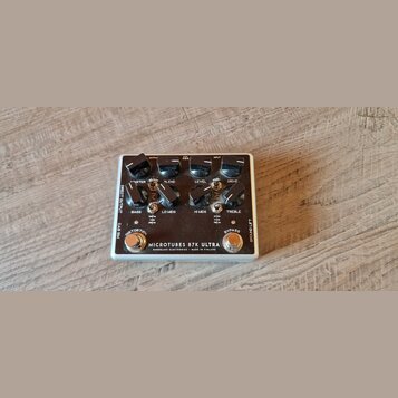 Kytarový efekt pedál v bílém kovovém šasi. Na horní straně je nápis MICROTUBES B7K ULTRA, DARKGLASS ELECTRONICS - MADE IN FINLAND. Pedál má dva spína…