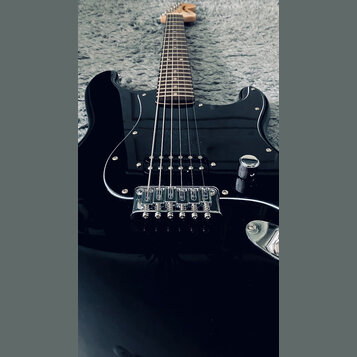 Černá elektrická kytara s tvarem typu Stratocaster a hnědým hmatníkem. Nástroj má jeden viditelný snímač typu humbucker v pozici u mostu a chromovaný…