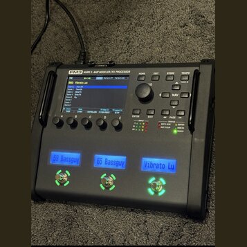 Černý kytarový procesor s nápisem FM3 MARK II - AMP MODELER/FX PROCESSOR. Zařízení má displej, ovládací knoflík a tři podsvícená tlačítka s nápisy 59…