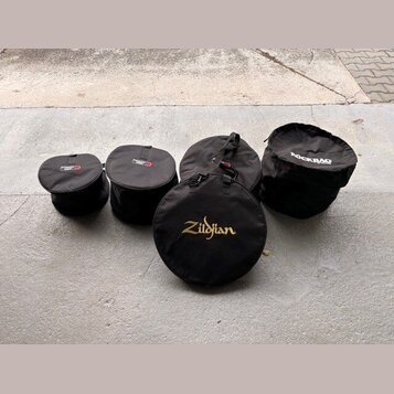 Pět černých textilních přepravních tašek na činely v různých velikostech. Na jedné z tašek je zlatý nápis Zildjian, na jiné bílý nápis ROCKBAG a na d…