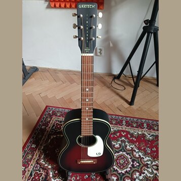 Akustická kytara s černým povrchem a červeným přechodem v oblasti středu. Na hlavě je bílý nápis GREISCH® a pod ním svisle napsaný model JIM + DANDY,…