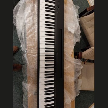 Černý digitální klavír s bílými a černými klávesami. Na pravé straně korpusu je viditelný nápis YAMAHA. Nástroj leží na dřevěném povrchu a je částečn…