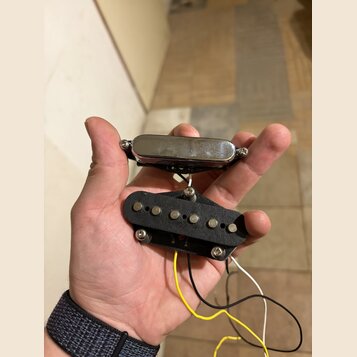 Fotografie zachycuje dva elektrické kytarové snímače držené v dlani. Horní snímač je typu humbucker s chromovaným krytem, spodní je jednoduchý snímač…