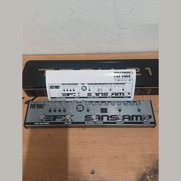 Kytarový efekt pedál stříbrné barvy s nápisy TECH 21 Fly RIG, EFX a SANSAMP. Na spodní straně jsou označení TAP/REVERB, DELAY, BLONDE/TUNER, BOOST a…