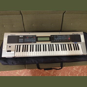 Stříbrný digitální klavír s nápisy Roland a PRELUDE. Nástroj má standardní klávesnici, LCD displej uprostřed a několik ovládacích tlačítek v sekcích…