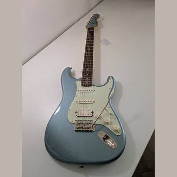 Modrá elektro kytara s kovovými stupeničky a bílým pickguardem. Na hlavě je viditelné logo Fender. Nástroj má tři snímače, tři ovládací knoflíky a tř…