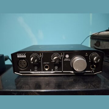 Černý zvukový interface s nápisy ONYX a Artist 1-2. Na přední straně jsou dva knofíky GAIN, jeden velký knofík MONITOR a přepínače +48V, LINE/INST a…