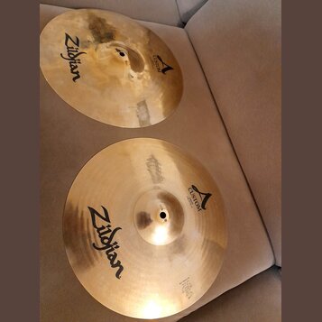 Dvě mosazné činely značky Zildjian. Oba mají nápis CUSTOM a logo ve tvaru písmena A. Spodní činel má v dolní části drobný nečitelný text a technické…
