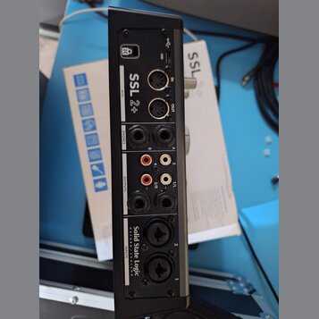 Zadní strana černého audio rozhraní s nápisy SSL 2+ a Solid State Logic. Jsou zde viditelné konektory USB, MIDI IN a OUT, dva výjemy PHONES, pět OUTP…