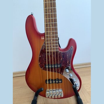 Čtyřstrunná elektrická basová kytara s červeným gradientním lakem a hnědým dřevěným povrchem. Nástroj má tmavý vzorovaný pickguard, dva snímače a tři…