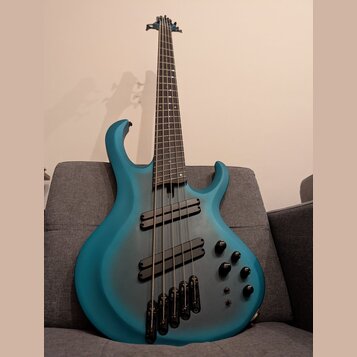 Modrá basová kytara s pětistrunným hmatníkem a dvěma humbuckery. Tělo má matný povrch s tmavším stínováním v oblasti středové části. Na těle jsou umí…