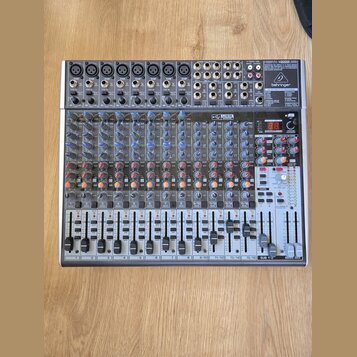 Stříbrný mixážní pult značky behringer s označením XENYX 2442USB. Zařízení obsahuje numerous vstupní konektory, posuvníky a ovládací knoflíky v modré…