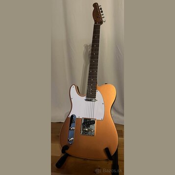 Kytara typu Telecaster v matné bronzové barvě s bílým pickguardem. Na krytu snímače je viditelný nápis "Fender". Nástroj je umístěn na černém stojanu.