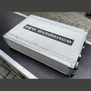 Stříbrný transportní kufr z hliníku s texturovaným povrchem. Uprostřed je černý nápis pro evidence. Povrch vykazuje známky opotřebení v podobě škrába…