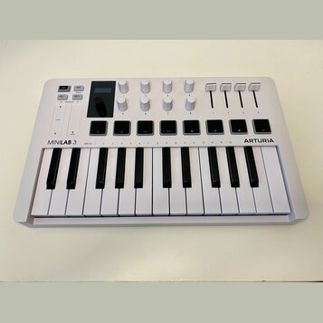 Bílá klaviatura s nápisy MINILAB 3 a ARTURIA. Horní panel obsahuje osm otočných knoflíků, čtyři posuvníky a osm čtvercových tlačítek. V levé části js…
