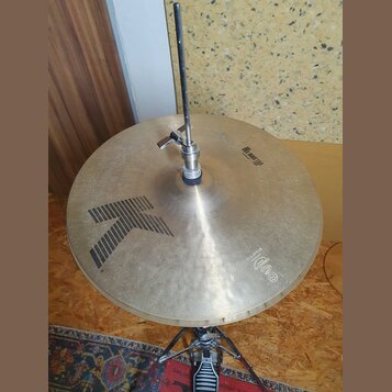 Kruhové činely z mosazného kovu s viditelným broušením povrchu. Na ploše je černý grafický symbol šipky a nápisy „Hi Hat TOP“ oraz „14" 105Hz L21“. V…