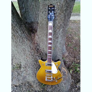 Zlatá elektrická kytara s černým hmatníkem a bílými vložkami. Na hlavě je nápis GRETSCH, na těle se nachází bílý plechtrguard a nápis GRETSCH. Nástro…