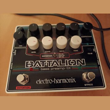 Kytarový efekt v černém provedení s bílým rámem. Na přístroji je nápis BATTALION bass preamp+ DI a značka electro-harmonix. Obsahuje šest černých hor…