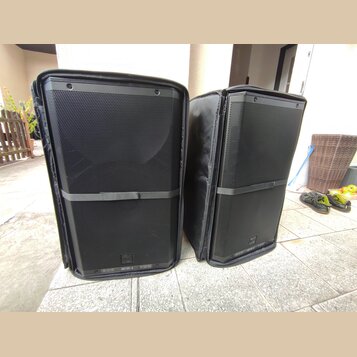 Dvě černé reproduktorové bedny v černých přepravních brašlech. Na spodní hraně levého reproduktoru je viditelný nápis ART 915-A. Povrch mřížek je v d…