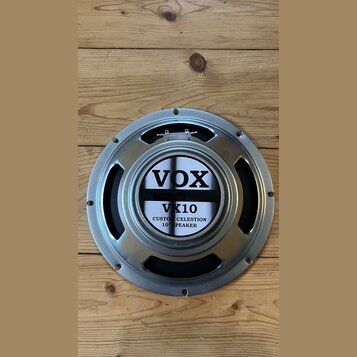 Kruhové reproduktory s kovovým rámem v stříbrné barvě. Uprostřed je štít s nápisy VOX, VX10 a CUSTOM CELESTION 10" SPEAKER. Povrch rámu vykazuje drob…