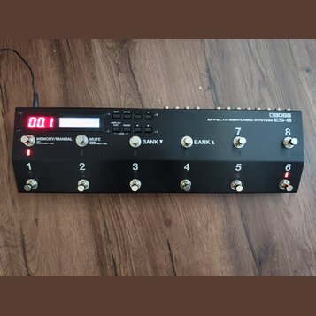 Černý efektový spínací systém s nápisem BOSS EFFECTS SWITCHING SYSTEM ES-8. Zařízení má digitální displej zobrazující červeně číslo 00.1 a osm kovový…