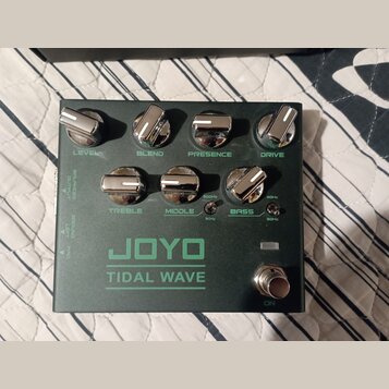 Tmavě zelený kytarový efekt s nápisem JOYO TIDAL WAVE. Na horní straně jsou čtyři chromované ovratovky s popisky LEVEL, BLEND, PRESENCE a DRIVE. Ve s…
