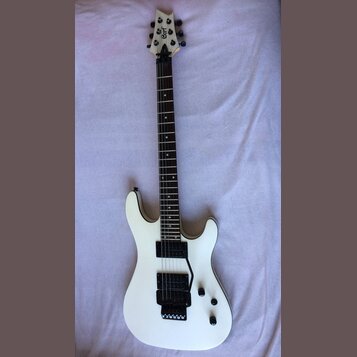 Bílá elektrická kytara s tmavým hmatníkem a dvěma humbuckery. Na hlavě je viditelné logo Cort. Nástroj vykazuje známky používání v podobě drobných šk…