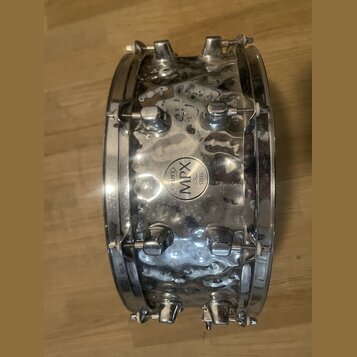 Stříbrný kovový snare drum s chromovaným povrchem. Uprostřed korpusu je kulatý štítek s nápisy MAPEX a MPX STEEL. Povrch nástroje vykazuje výrazné zn…
