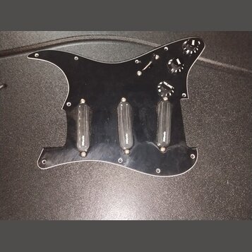 Černý plastový pickguard pro kytaru s třemi černými snímači. Na každém ze snímačů je bílý nápis "Wilkinson". Součástí jsou tři černé ovládací knofíky…