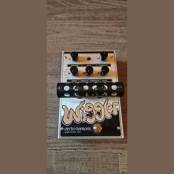 Kytarový efekt s bílým kovovým šasi a černými ovládacími knoflíky. Na spodní části je velký nápis Wiggler a logo electro-harmonix s textem MADE IN NY…