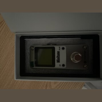Kompaktní digitální ladička v bílém obalu s pěnovou výplní. Na přístroji je nápis Minitune a označení A4 FLAT, v pravé části je logo revoltage. Zaříz…