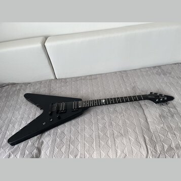 Černá elektrická kytara s tělem ve tvaru V. Na hlavě je bílé logo Epiphone a nápis Authorized Dealer. Hриф má v horní části bílou inlaidaci ve tvaru…