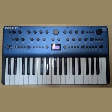 Modré synthesizátory s klaviaturaí. Na horním panelu je vlevo nápis COBALT 8 a uprostřed pod displejem značka MODAL ELECTRONICS, vpravo je logo M. Př…