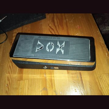 Černý kompaktní zesilovač s kovovým vrškem a texturovaným spodním tělem. Na horní straně je vyfrézovaný nápis AMPLIFIER a výrazné logo VOX. Povrch vy…