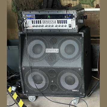 Fotografie zobrazuje basový zesilovač a reproduktorovou skříň v černém provedení. Na horním zařízení je nápis FENDER BASS AMPLIFICATION a pod ním ozn…