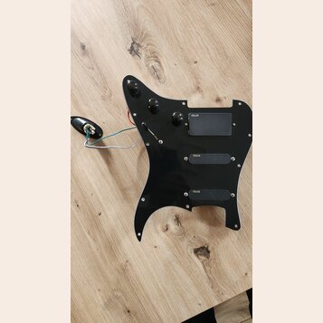 Černý plastový pickguard s třemi integrovanými snímači. Na každém ze snímačů je viditelný nápis emg. Součástí jsou tři černé ovládací knoflíky, přepí…