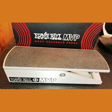 Kytarový pedál s hliníkovým šasi a hrubou, protiskluzovou povrchovou úpravou na horní části. Na boku je uveden nápis ERNIE BALL MVP. V pozadí je vidě…