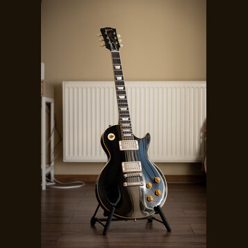 Černá elektrická kytara s jednovýstupním tělem a hnědým lemováním. Na hlavě je zlatý nápis Gibson. Kytara má dva humbuckery, čtyři otočné knoflíky a…