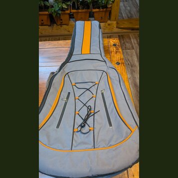 Šedý pol pevný pouzdro na kytaru s oranžovými detaily a lemováním. Na přední straně jsou dvě zipové kapsy a šňůrování s černým stahovacím provázkem.…