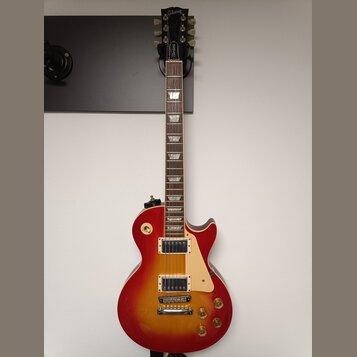 Elektrická kytara s červeným gradientním lakem (sunburst) a krámem z tmavého dřeva. Na hlavě je nápis Gibson a na hrazence nápis Standard. Nástroj má…
