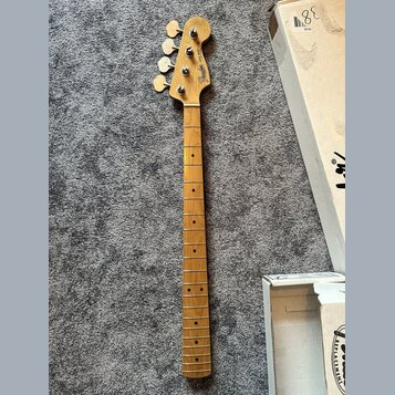 Hrabedlo basové kytary s přírodním dřevěným povrchem a hmatníkem z jasného dřeva. Na hlavě je viditelné logo Fender a nápis Jazz Bass. Nástroj vykazu…