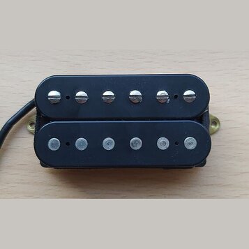 Černý humbucker s dvěma řadami šesti snímačů. Horní řada má viditelné šroubovací hlavy, spodní řada jsou hladké čepy. Na komponentu nejsou viditelné…