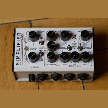 Bílý kytarový zesilovač s nápisem SIMPLIFIER MKII ZERO WATT REVERB STEREO AMPLIFIER. Zařízení obsahuje několik černých otočných potenciometrů a přepí…