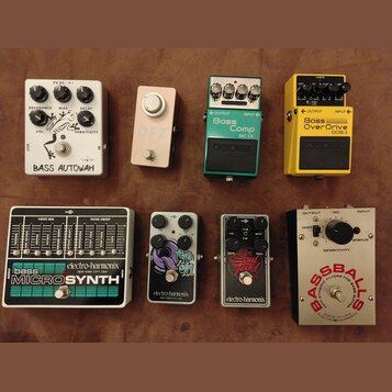 Fotografie zobrazuje osm kytarových efektů rozložených ve dvou řadách. V horní řadě jsou pedály s nápisy BASS AUTOWAH, DFZ, Boss Bass Comp BC-1X a Bo…