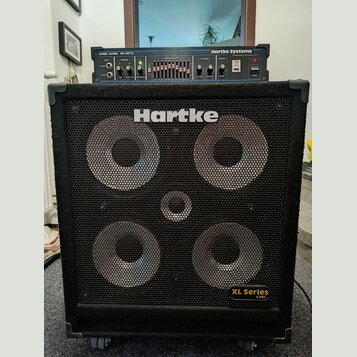 Černý basový reproduktor s kovovou mřížkou, na které je bílý nápis Hartke a v pravém dolním rohu žlutý štítek XL Series 4.5XL. Nad reproduktorem je u…