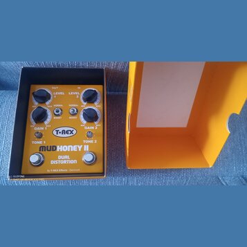 Kytarový efekt v oranžovém šasi s nápisy T-REX, MUDHONEY II a DUAL DISTORTION. Na spodní části je text By T-REX Effects Denmark. Zařízení má čtyři če…