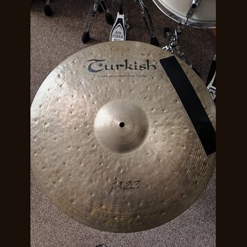 Kulatý mosazný činel s kovaným povrchem. Na horní části je černý nápis Turkish a pod ním text handmade cymbals from Turkey. Ve spodní části je rukopi…
