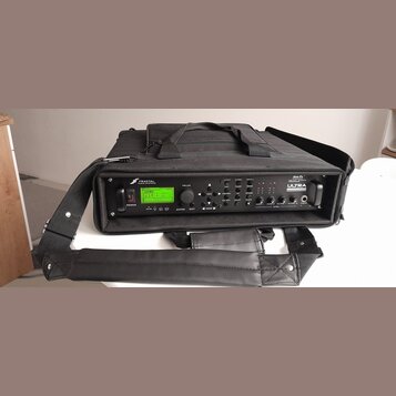 Černý rackový procesor v černé přepravní tašce s popruhem. Na předním panelu je zelený LCD displej a nápisy FRACTAL AUDIO SYSTEMS oraz Axe-Fx ULTRA.…