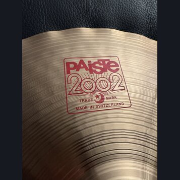 Detail činely z mosazi s koncentrickými rýhami. Na povrchu je červený nápis PAiste 2002, pod kterým je v rámečku text TRADE MARK a MADE IN SWITZERLAN…