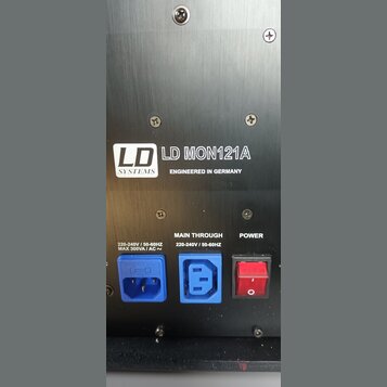 Detail zadní strany černého elektronického zařízení s kovovým povrchem. Je zde uveden nápis LD SYSTEMS, model LD MON121A a text ENGINEERED IN GERMANY…